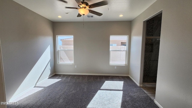 empty room with ceiling fan, plenty of natural light, and dark carpet