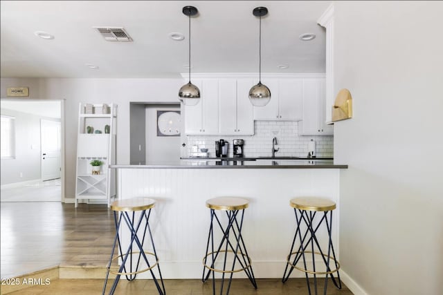 kitchen featuring dark hardwood / wood-style floors, decorative light fixtures, tasteful backsplash, white cabinets, and a kitchen breakfast bar