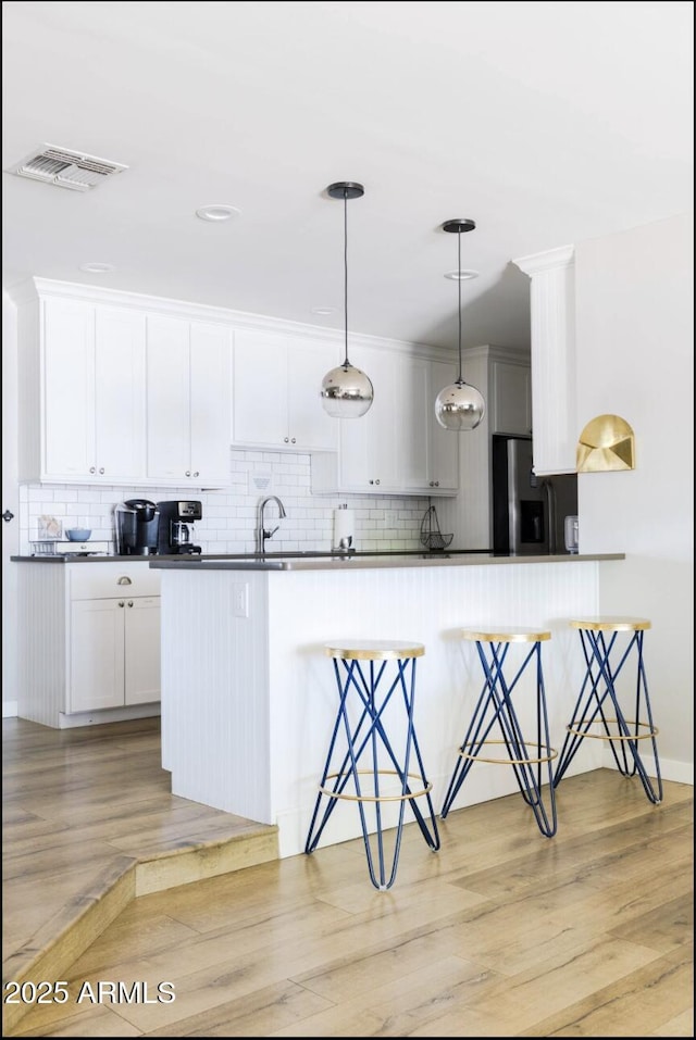 kitchen with light hardwood / wood-style flooring, pendant lighting, stainless steel refrigerator with ice dispenser, a kitchen bar, and white cabinetry