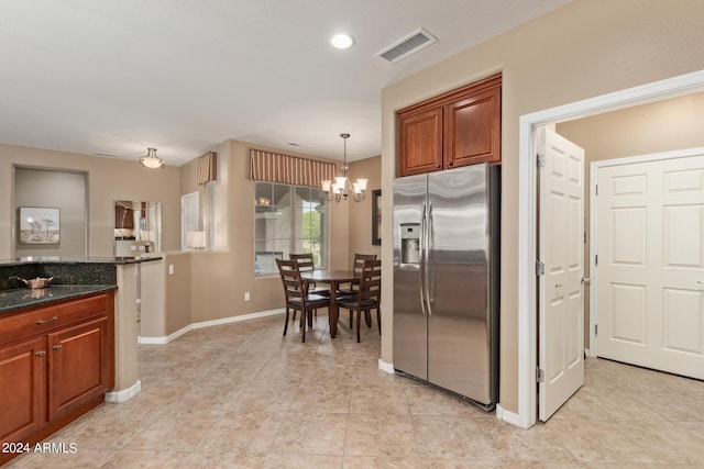 kitchen with a notable chandelier, stainless steel fridge, dark stone counters, and decorative light fixtures