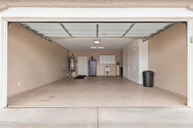 garage with black refrigerator, a garage door opener, sink, and gas water heater