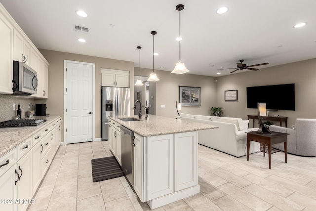 kitchen featuring white cabinets, ceiling fan, an island with sink, decorative light fixtures, and stainless steel appliances