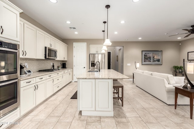 kitchen featuring light stone countertops, appliances with stainless steel finishes, white cabinets, hanging light fixtures, and an island with sink