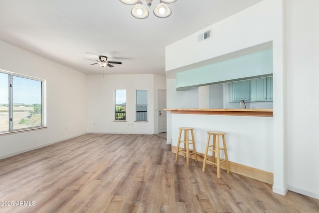 unfurnished living room featuring ceiling fan with notable chandelier, baseboards, visible vents, and light wood-style floors