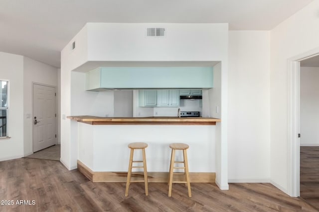 kitchen featuring stainless steel electric range oven, a peninsula, wood finished floors, and visible vents