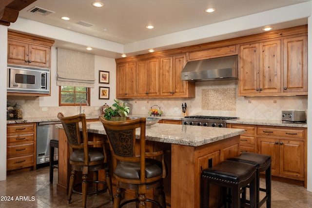 kitchen with a breakfast bar, wall chimney range hood, a kitchen island, appliances with stainless steel finishes, and decorative backsplash