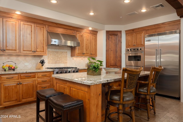 kitchen with wall chimney range hood, a center island, appliances with stainless steel finishes, and a kitchen bar