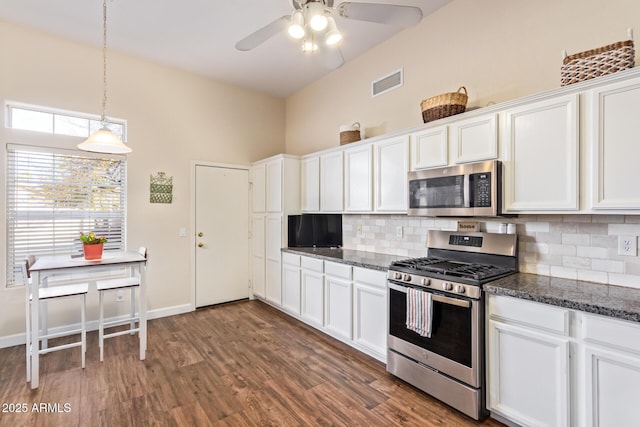 kitchen with dark wood-type flooring, white cabinetry, appliances with stainless steel finishes, dark stone counters, and decorative backsplash