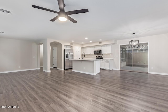 unfurnished living room with dark wood-style floors, baseboards, visible vents, and ceiling fan with notable chandelier