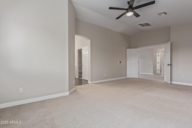 empty room with arched walkways, light carpet, visible vents, and baseboards