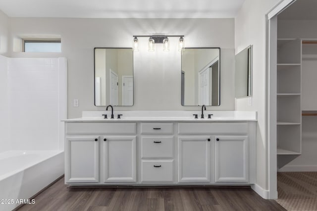 full bathroom with double vanity, wood finished floors, a sink, and baseboards