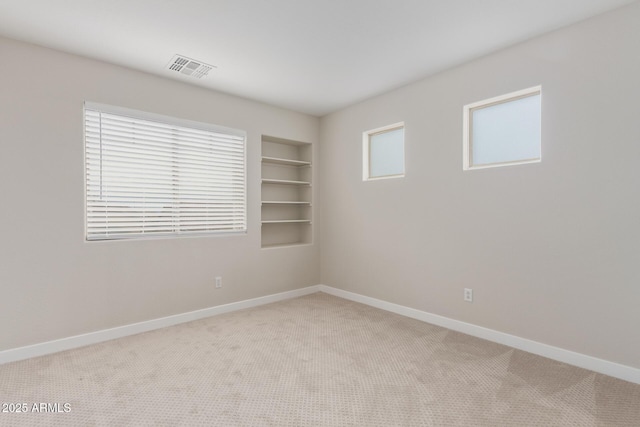 spare room with baseboards, visible vents, built in features, and light colored carpet