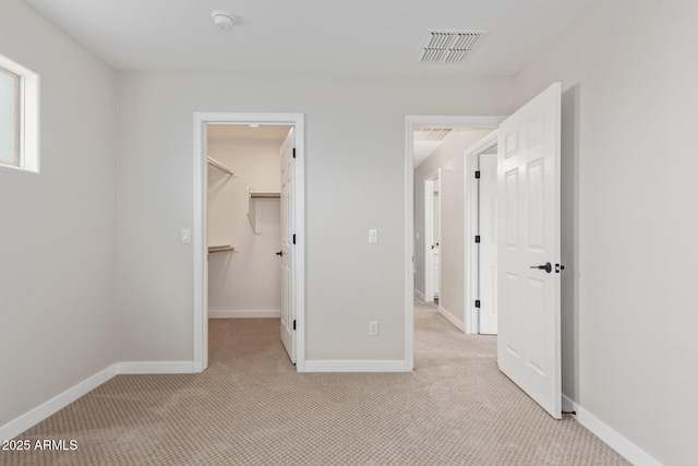 unfurnished bedroom featuring a walk in closet, visible vents, light carpet, and baseboards