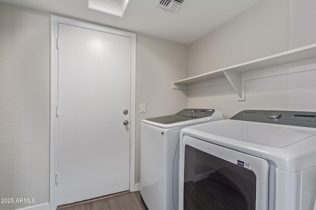 laundry room with laundry area, washer and clothes dryer, wood finished floors, and visible vents