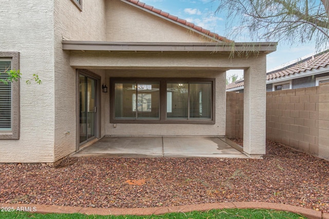 entrance to property with a tiled roof, fence, a patio, and stucco siding