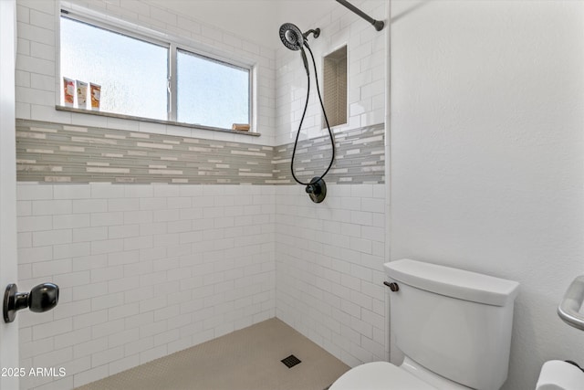 bathroom featuring tiled shower, toilet, and a wealth of natural light