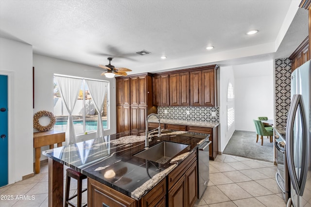 kitchen with tasteful backsplash, an island with sink, sink, and light tile patterned floors