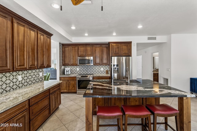 kitchen featuring a large island, light tile patterned floors, dark stone countertops, stainless steel appliances, and a kitchen breakfast bar