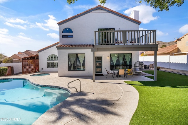 rear view of property with a swimming pool with hot tub, a lawn, a patio, and a balcony