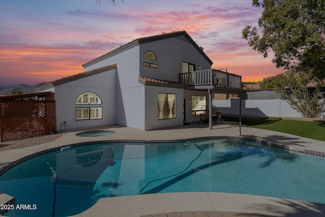 back house at dusk featuring a swimming pool with hot tub, a patio area, and a balcony