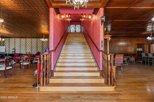 stairway featuring hardwood / wood-style flooring, wood walls, and a notable chandelier