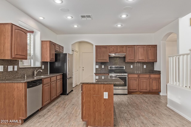 16215 W Durango St, Goodyear, AZ 85338 - kitchen featuring appliances with stainless steel finishes, under cabinet range hood, arched walkways, a center island, and dark stone counters