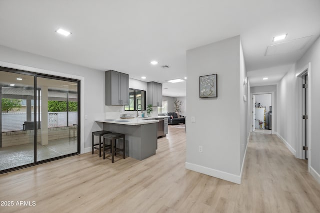 kitchen featuring light countertops, a kitchen breakfast bar, gray cabinets, a peninsula, and light wood-type flooring