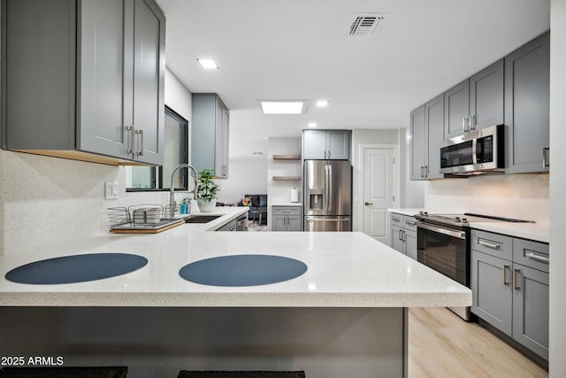 kitchen with gray cabinets, visible vents, appliances with stainless steel finishes, a sink, and light stone counters