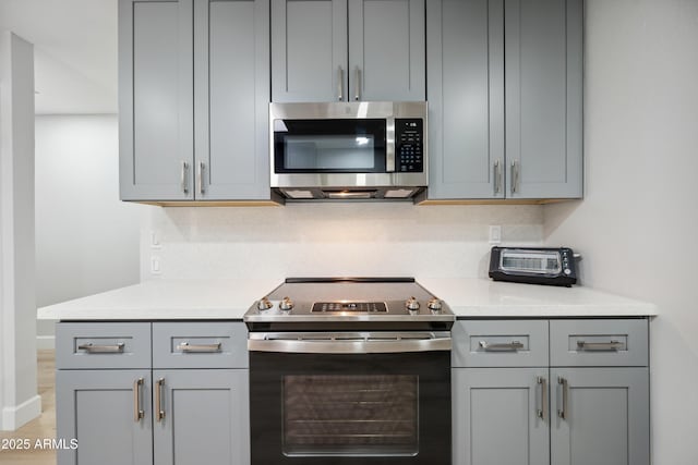 kitchen with light countertops, appliances with stainless steel finishes, a toaster, and gray cabinetry