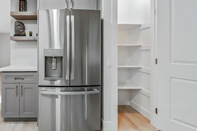 kitchen with stainless steel refrigerator with ice dispenser, open shelves, gray cabinets, and light wood finished floors