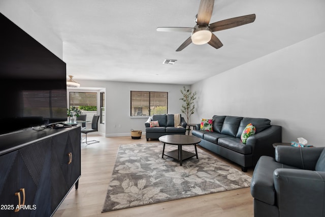living room with ceiling fan, visible vents, baseboards, and light wood-type flooring