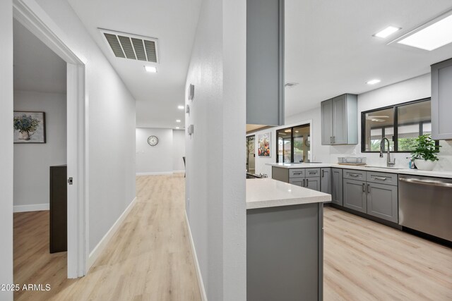 kitchen with a sink, light wood finished floors, dishwasher, gray cabinets, and visible vents