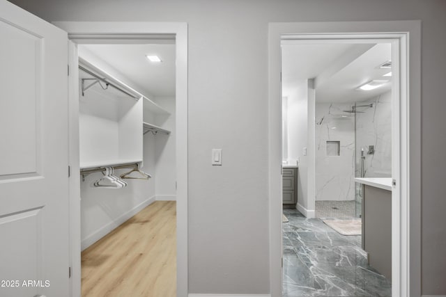 interior space with a walk in closet, baseboards, and a marble finish shower