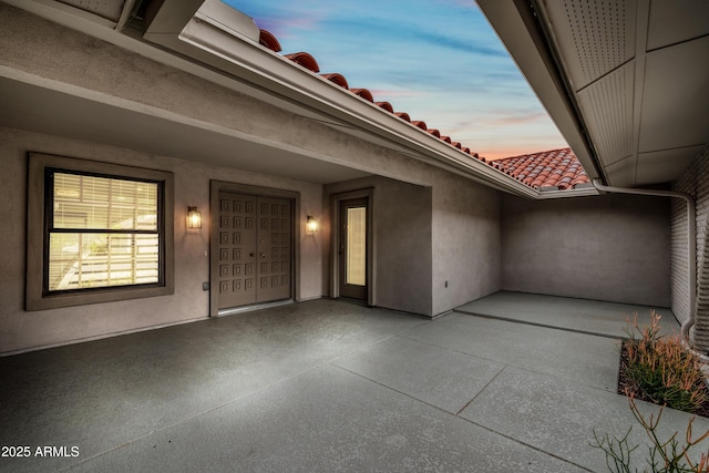 property entrance with a patio, a tiled roof, and stucco siding
