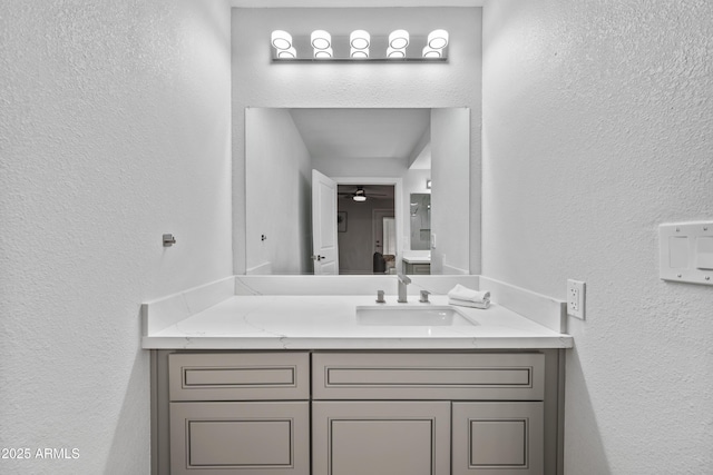 bathroom with a textured wall, ceiling fan, and vanity