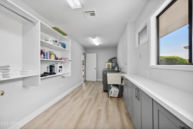 clothes washing area with a sink, washer / clothes dryer, baseboards, light wood-type flooring, and visible vents