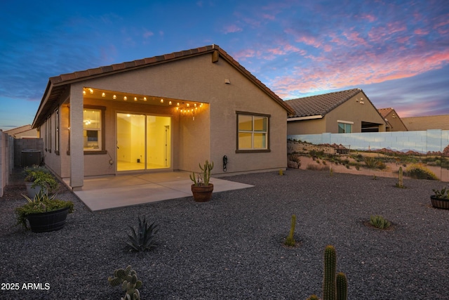 back of house at dusk featuring a tiled roof, central AC unit, stucco siding, a fenced backyard, and a patio area