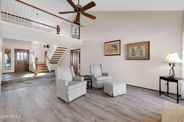 sitting room featuring ceiling fan, stairs, a high ceiling, and wood finished floors