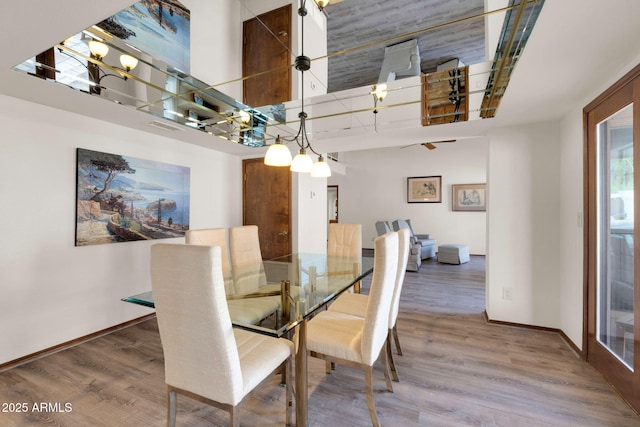 dining room featuring wood finished floors, baseboards, and a towering ceiling