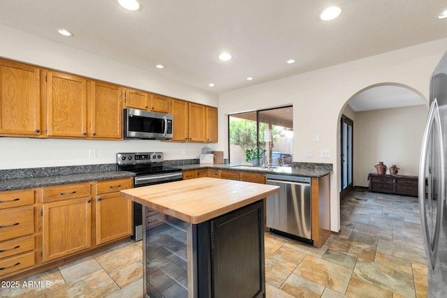 kitchen featuring a sink, wood counters, stone tile floors, stainless steel appliances, and arched walkways