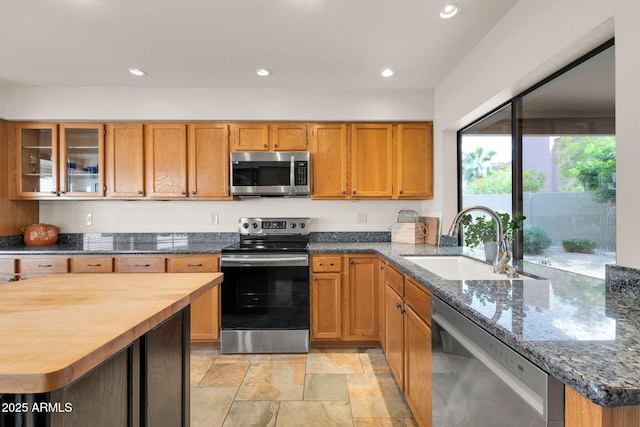 kitchen featuring dark stone countertops, recessed lighting, appliances with stainless steel finishes, brown cabinets, and a sink