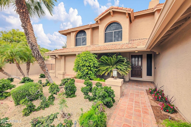 view of exterior entry with a tiled roof, fence, and stucco siding