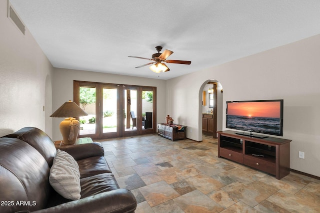 living room featuring visible vents, baseboards, french doors, arched walkways, and stone finish floor