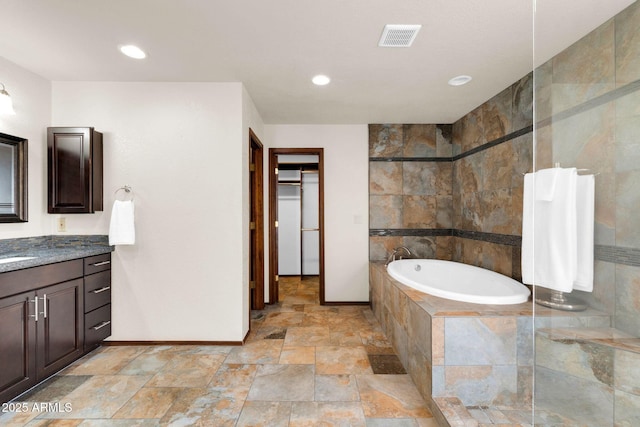 bathroom with a spacious closet, visible vents, baseboards, a bath, and stone finish floor