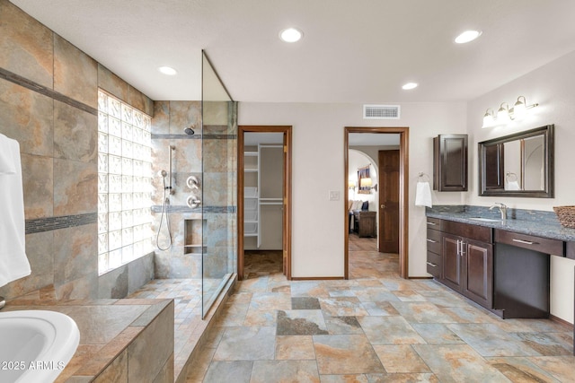 bathroom with vanity, a bath, visible vents, and a tile shower