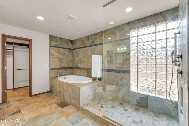 full bath with visible vents, a garden tub, stone tile flooring, and a walk in shower