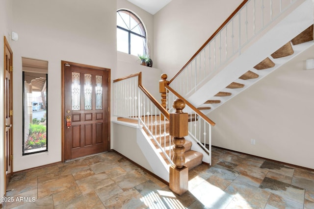 entrance foyer featuring stairway, baseboards, stone tile flooring, and a towering ceiling