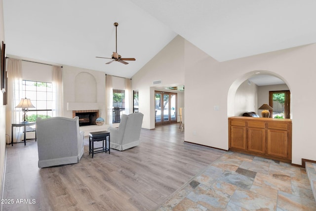 living room featuring visible vents, baseboards, high vaulted ceiling, a fireplace with raised hearth, and light wood-style floors