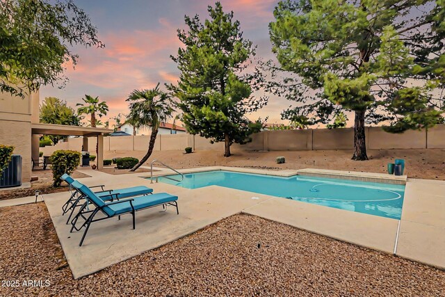 pool at dusk featuring a patio area, a fenced backyard, and a fenced in pool