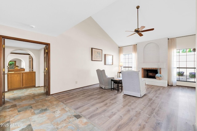 interior space with light wood-type flooring, high vaulted ceiling, ceiling fan, and a fireplace